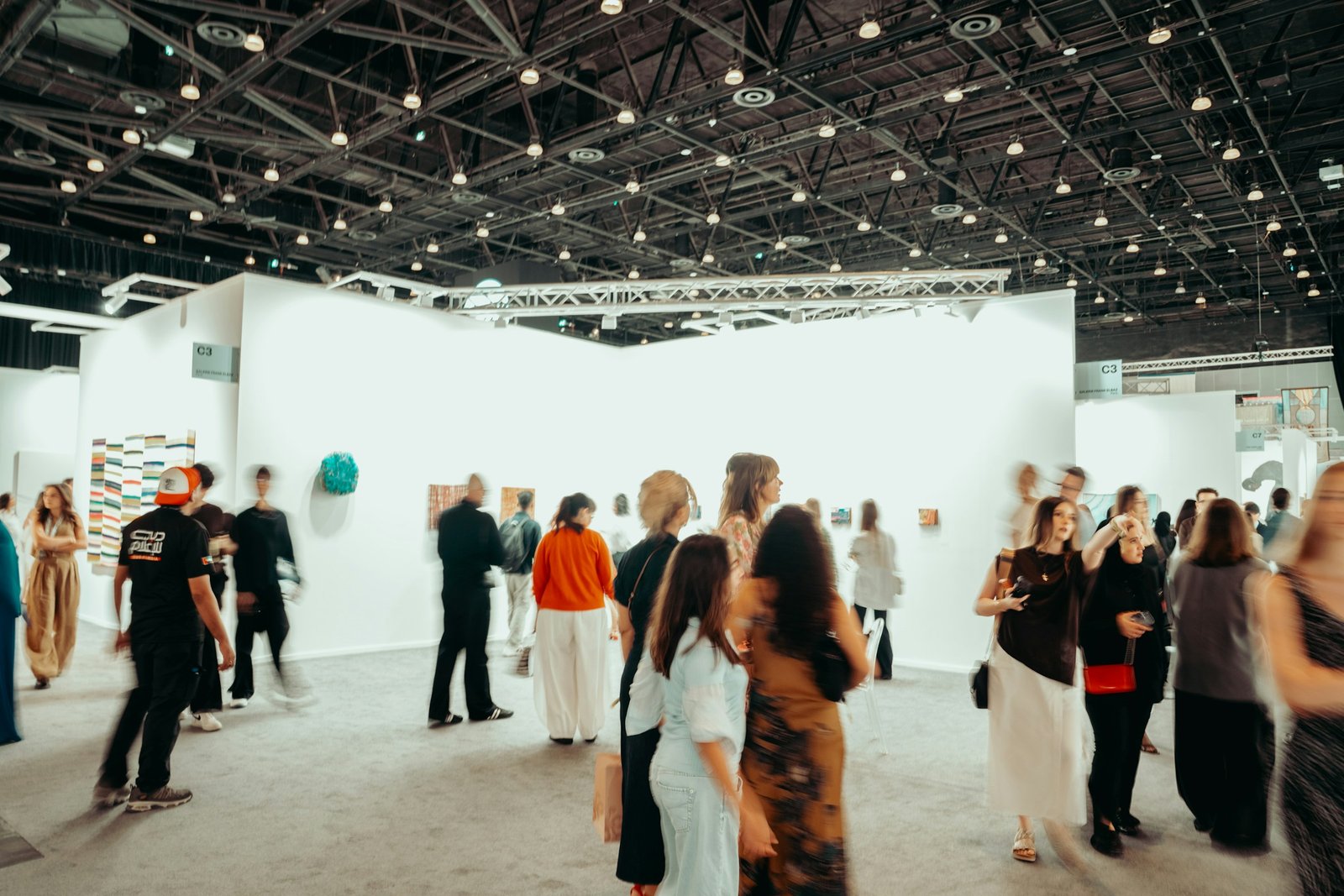 Visitors looking at large paintings in a bright art fair booth