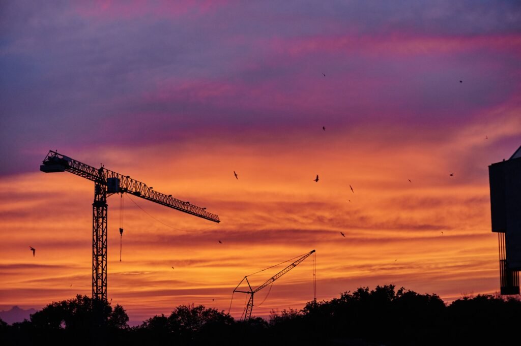 Tower cranes silhouetted against an evening sky