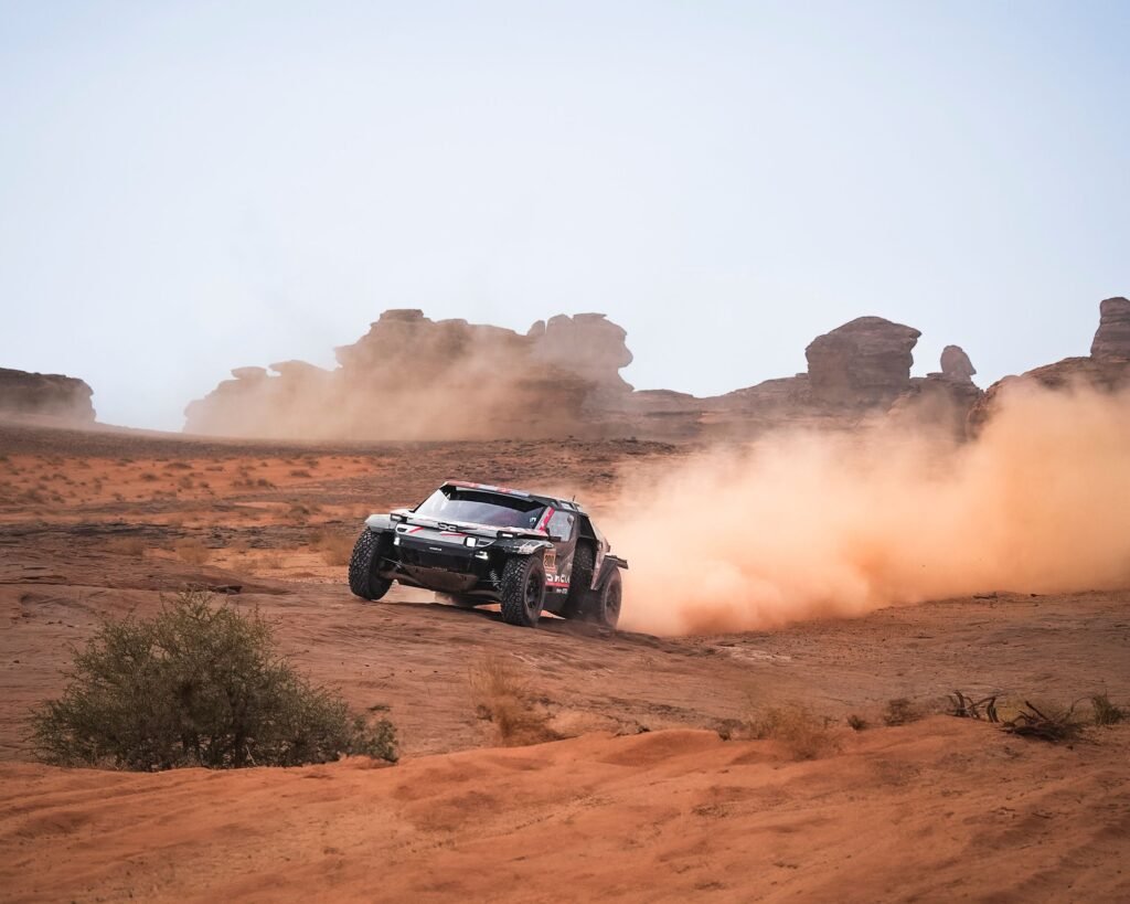 A rally vehicle throwing up sand as it crosses desert dunes