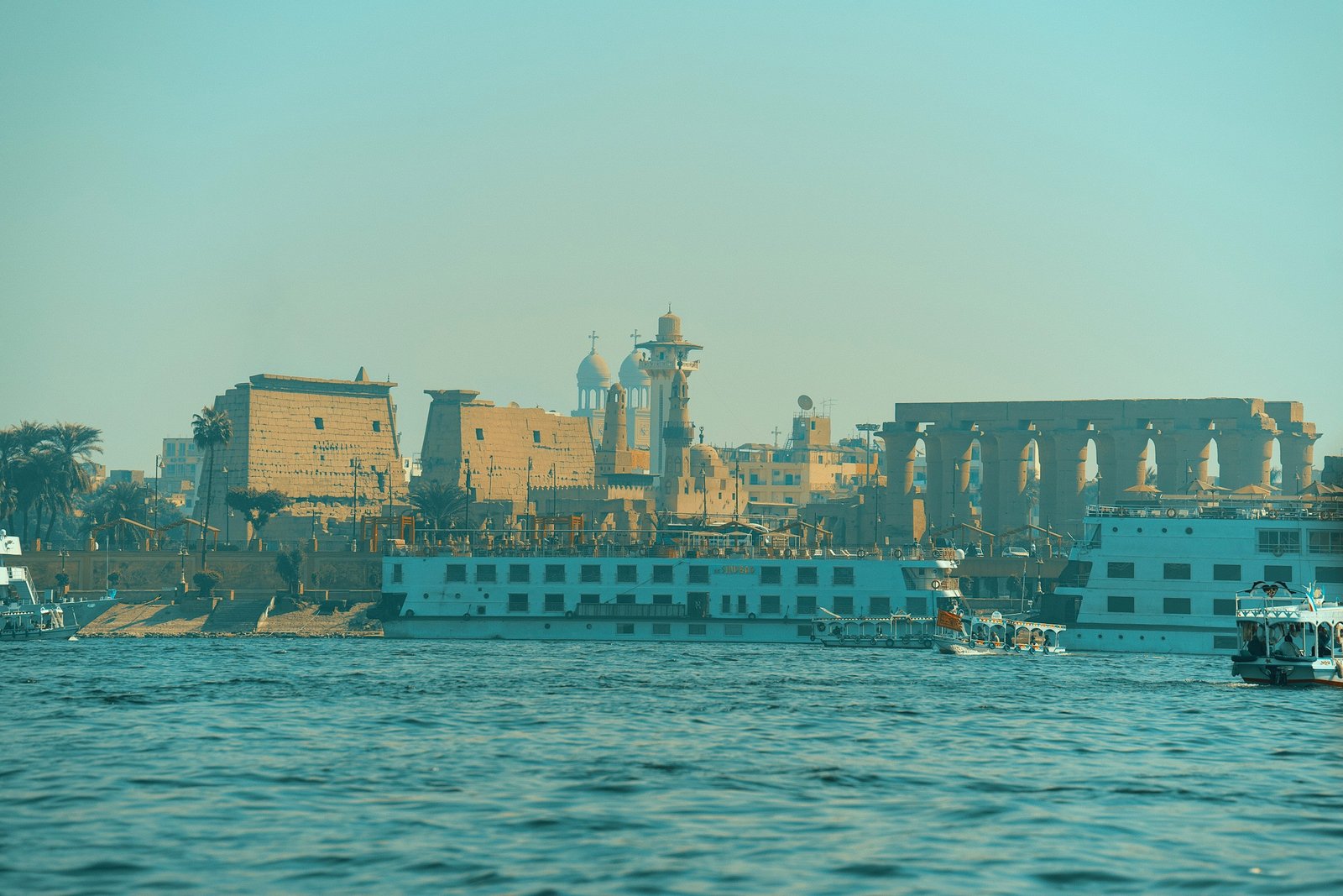 A river cruise boat on the Nile at sunset, with palm trees on the bank