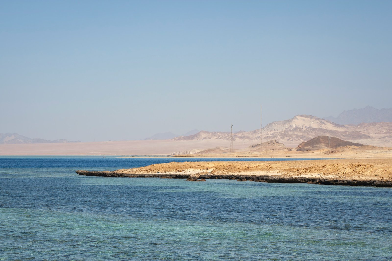 A pale sand beach and turquoise water with desert mountains behind