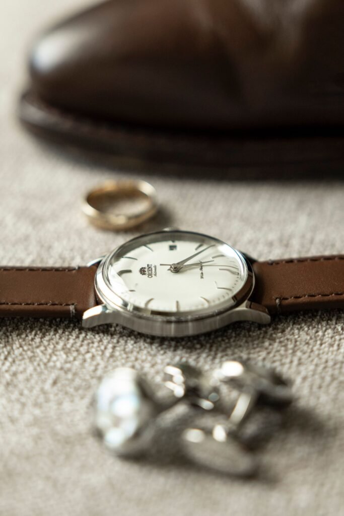 A classic watch laid out with a ring, a cufflink and formal shoes