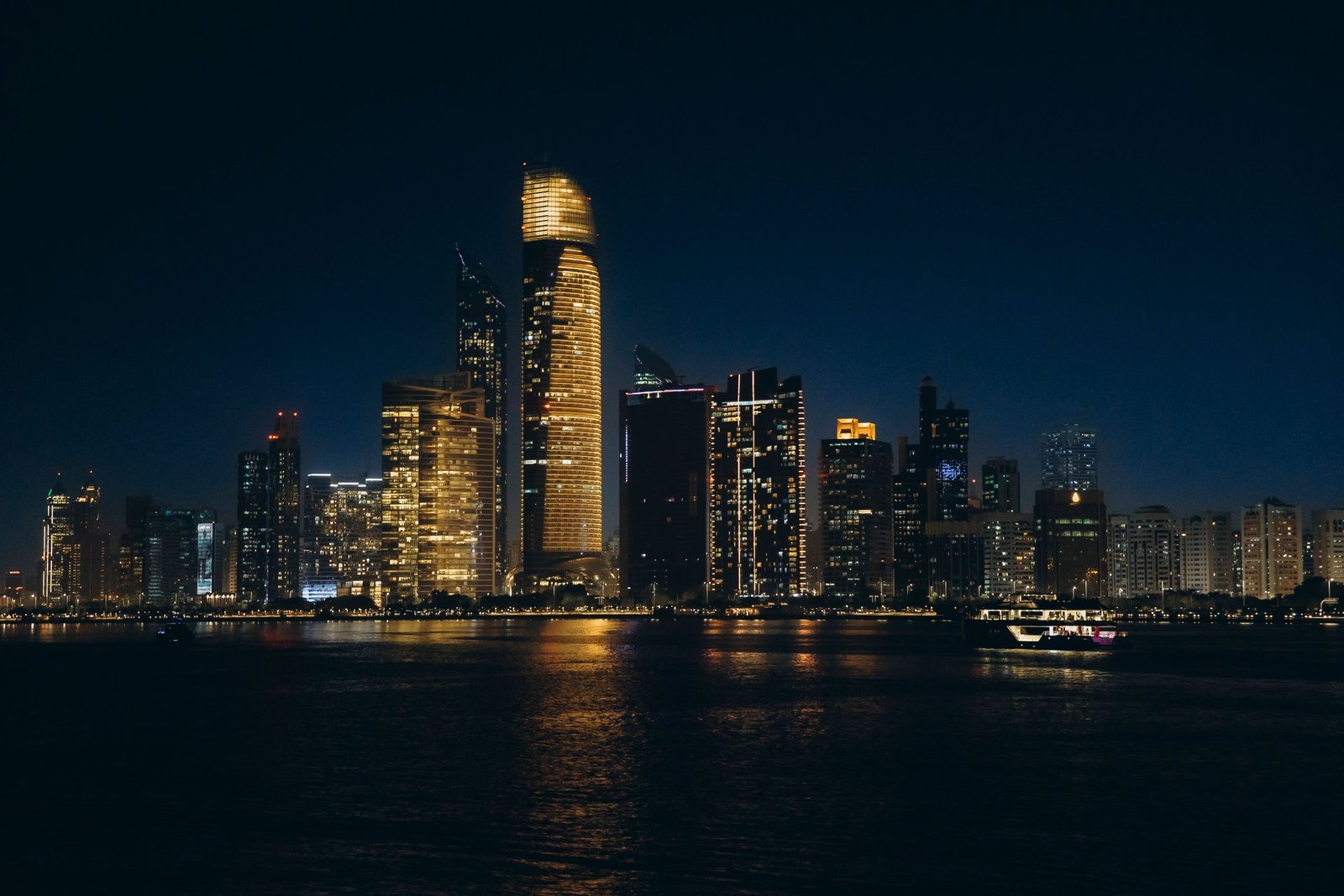 Abu Dhabi’s towers lit up at dusk above the waters of the Corniche